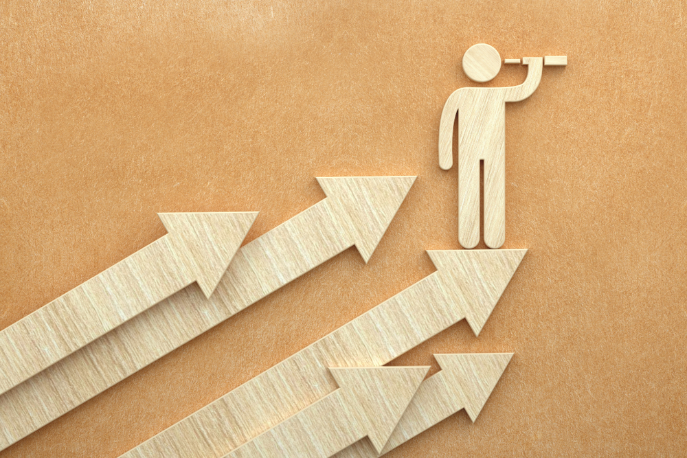 A wooden silhouette of a person stands on top of an upward‑pointing arrow and looks through a telescope. Several arrows point upward.