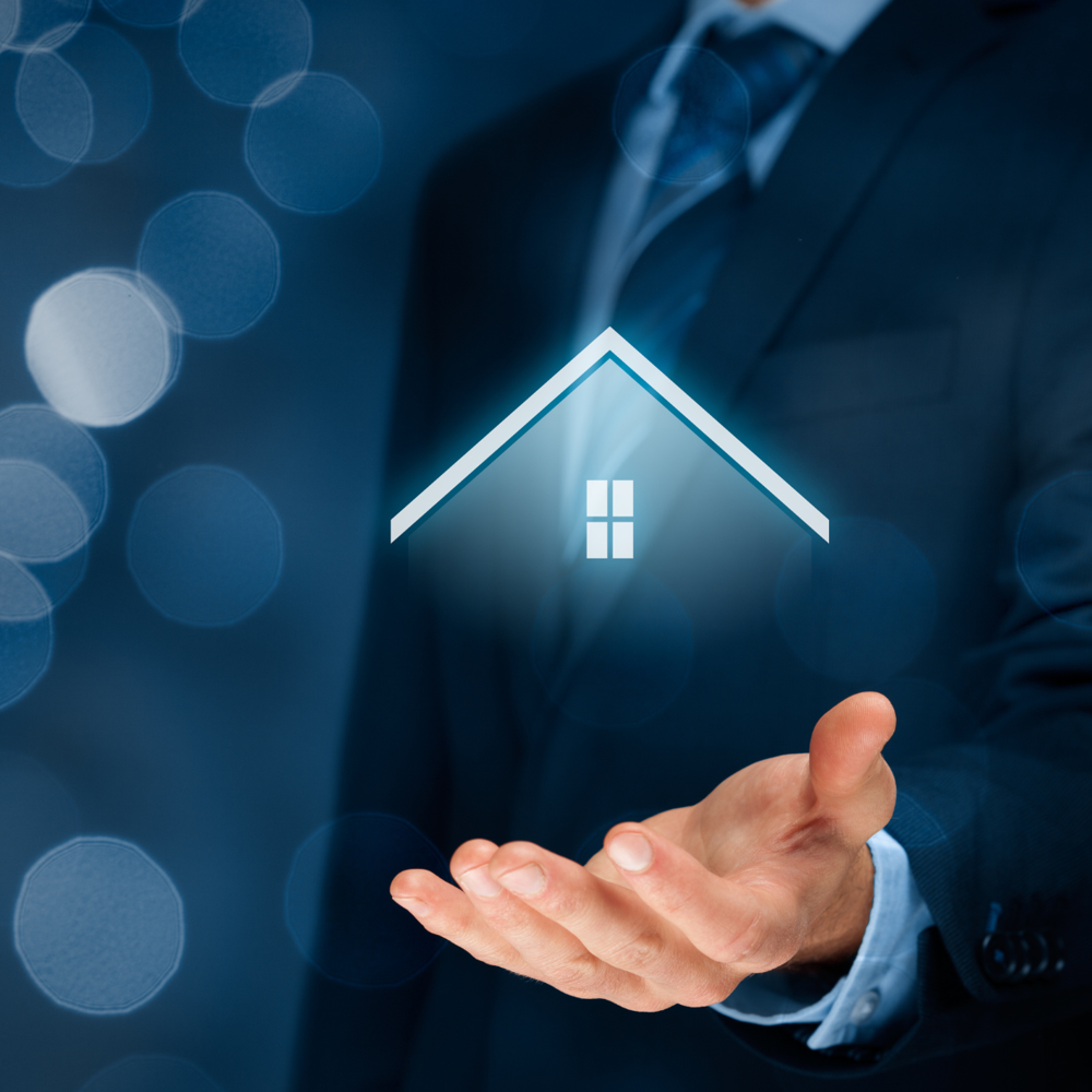 A person in business attire holding an open hand with a stylized house icon floating above it, illuminated in blue tones.