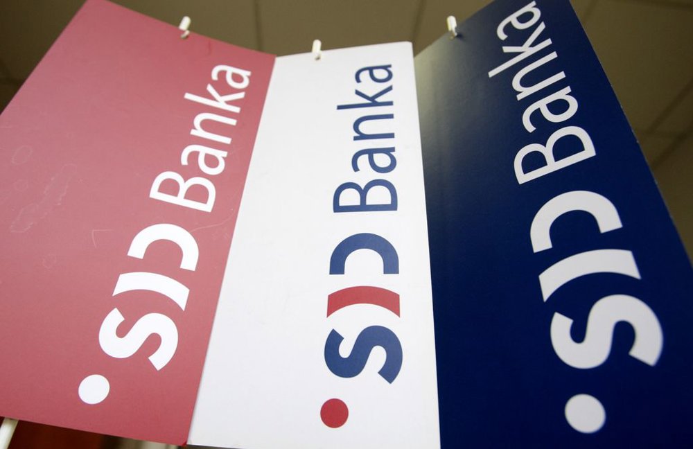 Tri viseče zastavice v rdeči, beli in modri barvi prikazujejo logotip in napis ‘SID banka’. Zastavice so postavljene pod različnimi koti in visijo s stropa.