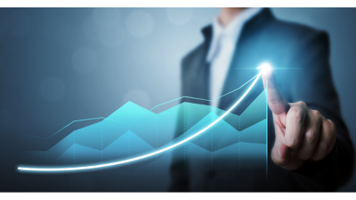 Oseba v poslovni obleki s prstom dotika svetleče točke na zaslonu, na katerem je prikazana navzgor usmerjena krivulja rasti in grafikon. Vizual ponazarja poslovno rast ali uspešnost.