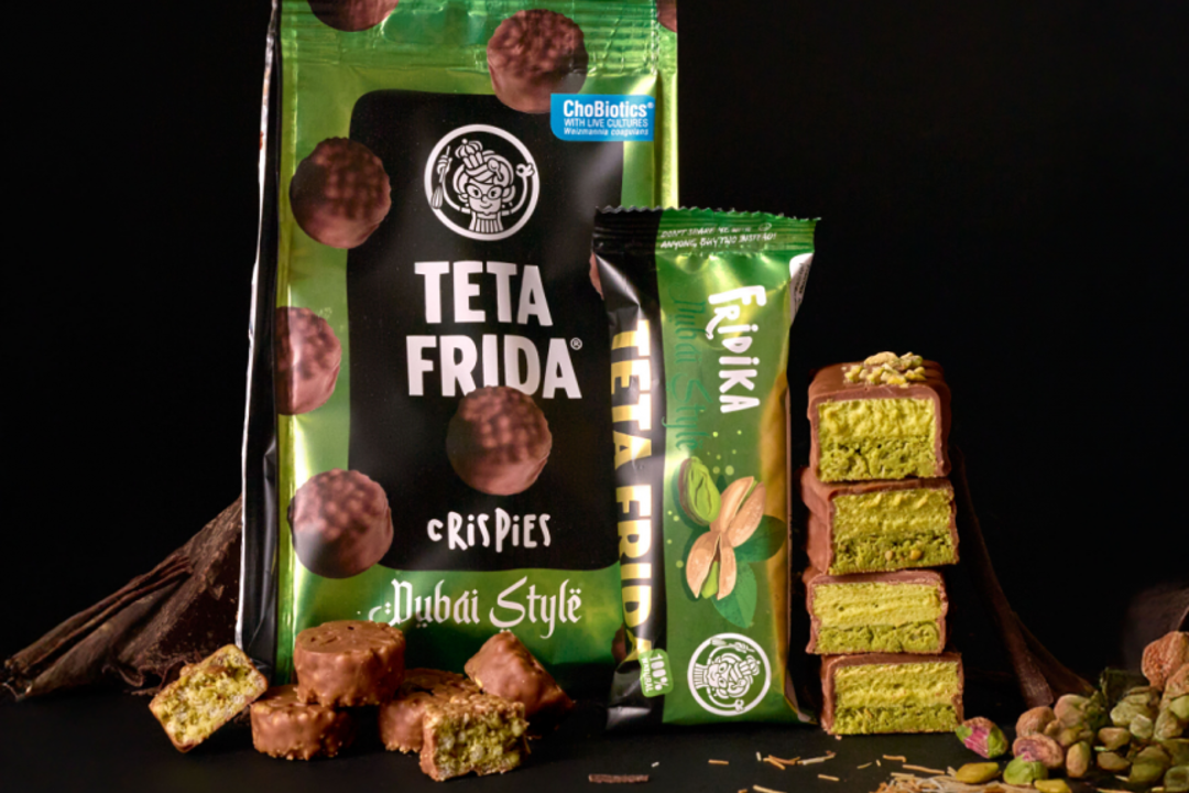 Packages of Teta Frida chocolate snacks and a green ReMix bar are displayed beside stacked pistachio pieces on a dark surface.