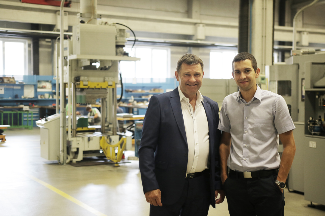 Two people standing in a manufacturing facility in front of a large industrial machine.