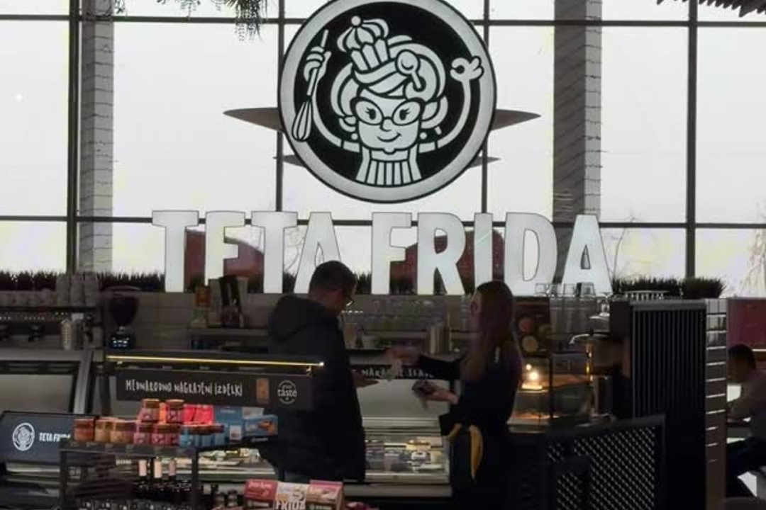 Interior of the Teta Frida shop with an illuminated logo above the counter, where two people stand near the dessert display.